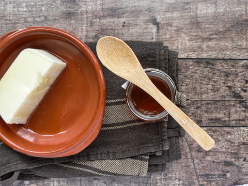A top view of fresh curd in a bowl with honey in a glass container and a wooden spoon on a table