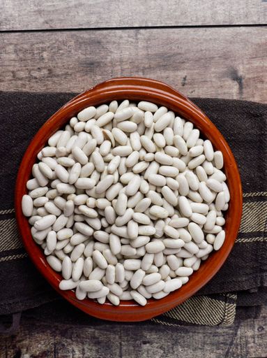 An overhead shot of white beans in a red bowl on a towel, laying on a wooden table