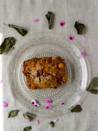 An overhead shot of a delicious casserole on a clear plate placed on a white surface, decorated with dry leaves and petals