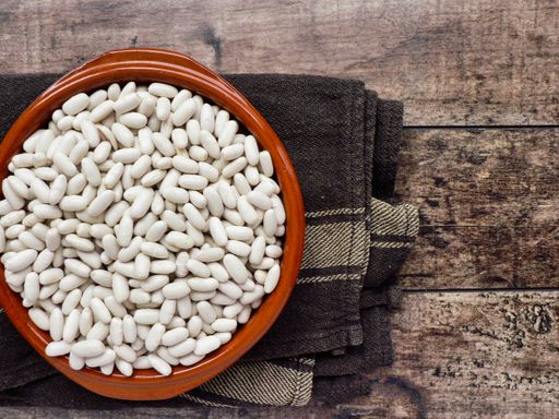 An overhead shot of white beans in a red bowl on a towel, laying on a wooden table