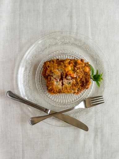 An overhead shot of a delicious casserole with a knife and fork on a clear plate, placed on a white surface