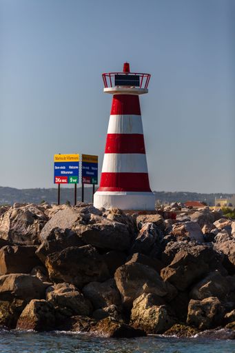 A vertical shot of a lighthouse on a rocky beach against a cloudless blue sky