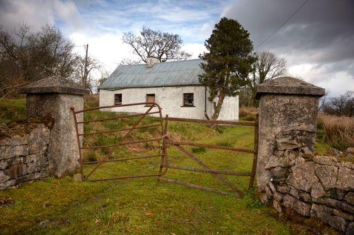 Old abandoned ruined building with grass covered yard against the cloudy sky