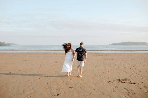 A backshot of a couple walking on the new River beach in daylight against the blue cloudy sky in New Brunswick, Canada