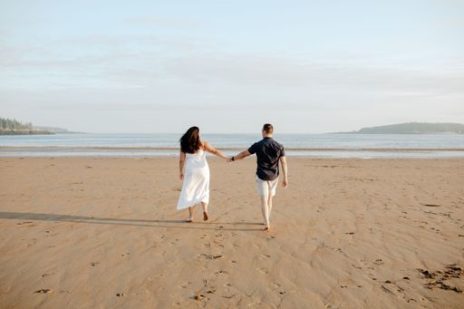 A backshot of a couple walking on the new River beach in daylight against the blue cloudy sky in New Brunswick, Canada
