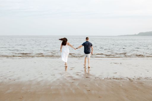 A backshot of a couple walking on the new River beach in daylight against the blue cloudy sky in New Brunswick, Canada