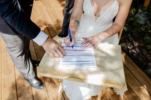 A closeup shot of a bride signing a wedding contract papers on a wooden table on a sunny day