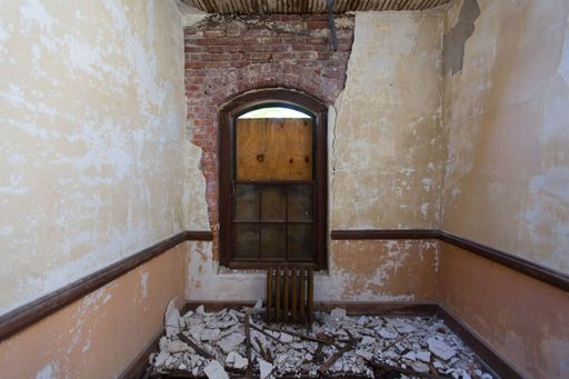 The interior view of an old room with damaged wall and floor with wooden window