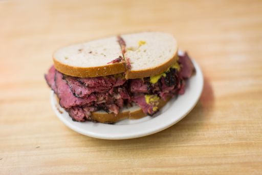 A closeup shot of pastrami sandwich in white dish on wooden surface