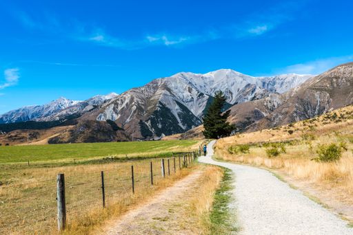 A narrow path next to a field leading to a rocky mountain in Cave Stream Scenic Reserve, South Island, New Zealand