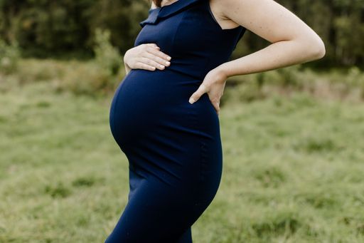 A young 38 weeks pregnant woman in a blue dress holding her belly