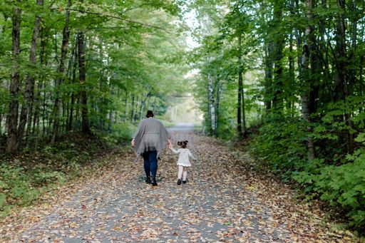 A back view of a mother with her daughter walking on a pathway covered in autumn foliage in a park