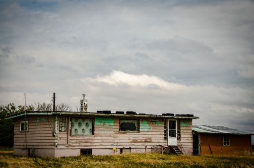 A creepy, old and aged abandoned wooden house in a field under the cloudy and rainy sky