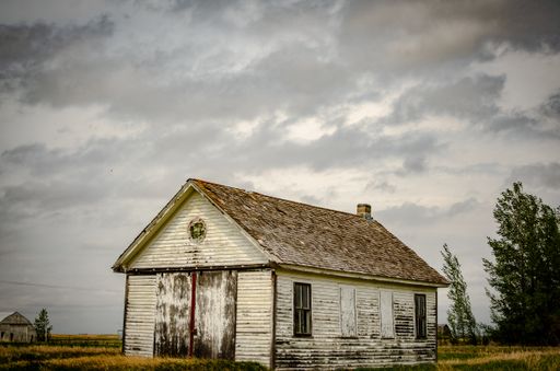 A creepy, old and aged abandoned house in a field under the cloudy and rainy sky