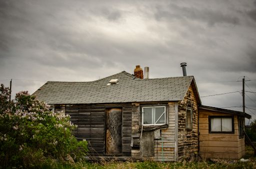A creepy, old and aged abandoned wooden house in a field under the cloudy and rainy sky