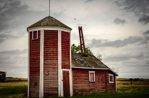 An old and aged abandoned red wooden house in a field under the cloudy and rainy sky