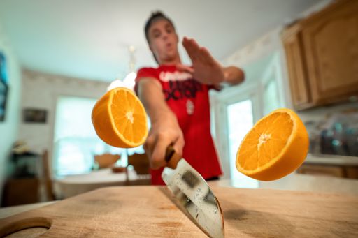 A closeup shot of the two halves of an orange in the air cut by a male in the background