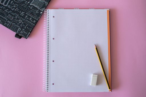 A high angle shot of a pencil and an eraser on a journal on a pink surface