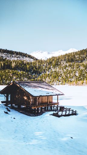 A vertical shot of a wooden house on the slope of a snow-covered mountain