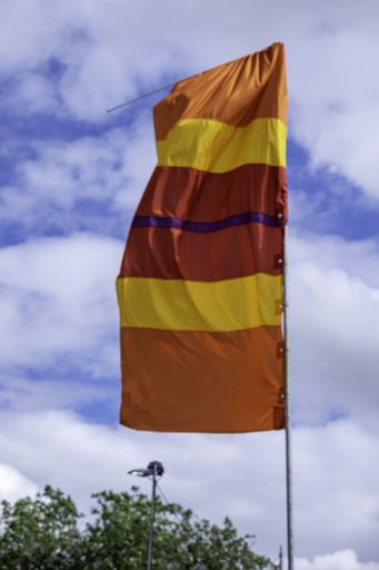 A vertical shot of a flag with red, orange, and yellow stripes at a music festival