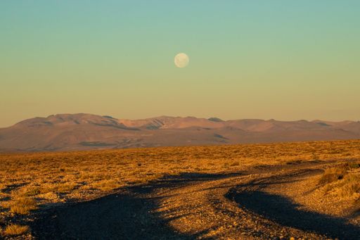 A dry orange field with small road near the mountain range on a cloudless sunset