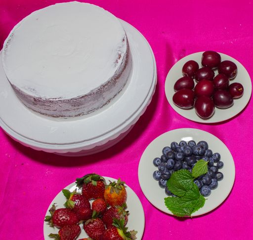 A cake with white cream and plates of various berries for the decoration