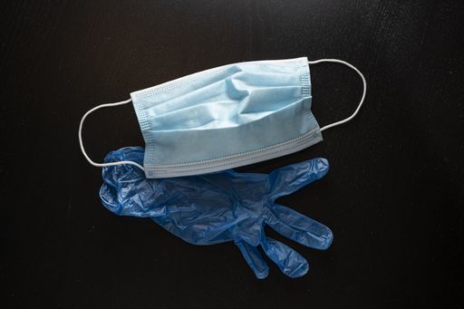 A protective face mask and a blue plastic glove on a black background