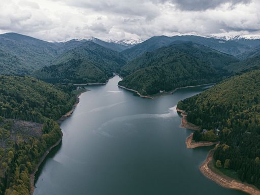 An aerial view of Vidraru Lake surrounded by lush forests in Arges County, Romania