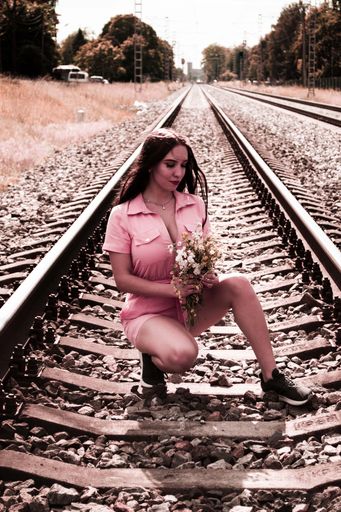 A Caucasian beautiful girl in pink outfit squats on train railway holding flowers