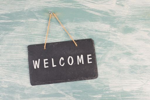 The word welcome is standing on a chalkboard sign, hanging on a blue textured weathered door, greeting to visiter