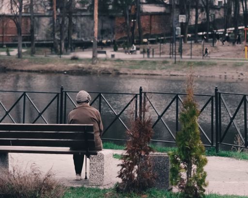 A close up elderly person sitting on a bench alone