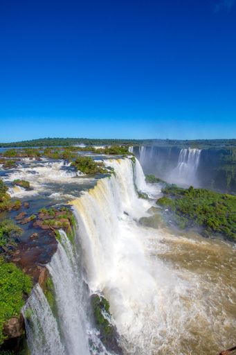 The Iguazu Falls in Brazil surrounded by trees under the blue sky
