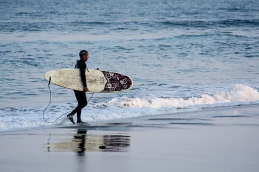 A male surfer carrying his surfboard on the beach of Malibu, California, USA