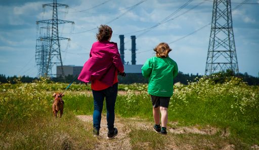 A landscape shot of people walking opposite of the wind with a dog