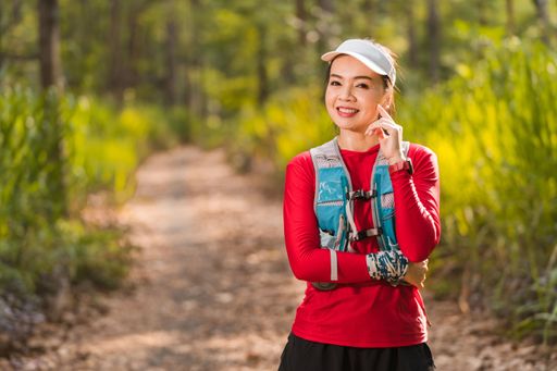 An Asian female wearing a running outfit in the middle of a trail