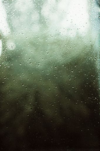 A vertical shot of the raindrops on the window behind a blurry background