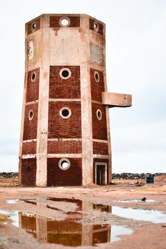An old tower made of red bricks against the cloudy sky in a field