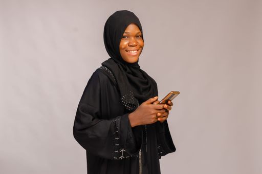 An African happy Muslim smiling lady using her phone and isolated on gray background