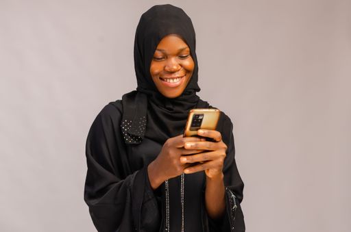 An African Muslim smiling excited lady using her phone and isolated on gray background