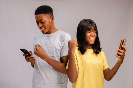 An excited African Couple standing feeling amazing and using phones isolated on gray background