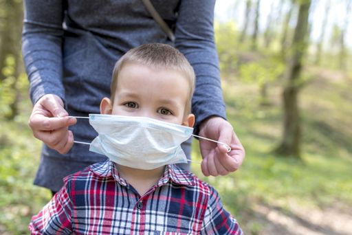 A little white boy's father helping him to wear a protective medical face mask for COVID-19 virus prevention
