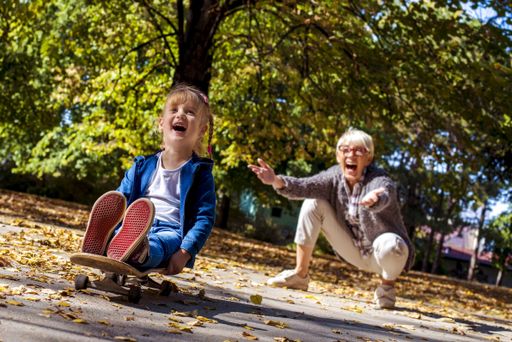 A cheerful little girl playing with her grandmother with a skateboard in a park