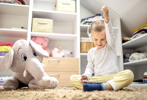 An adorable male child watching a video on a tablet with headphones and having fun in a playroom