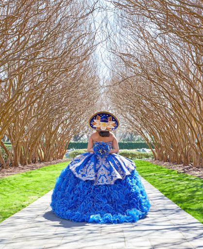 A vertical shot of a female posing in a forest in a blue Quinceanera Dress
