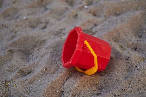 Closeup shot of red bucket beach toy with yellow handles on sand