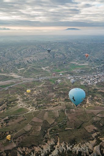 Colorful air balloons flying  over the fields and village houses at sunrise in Cappadocia, Turkey