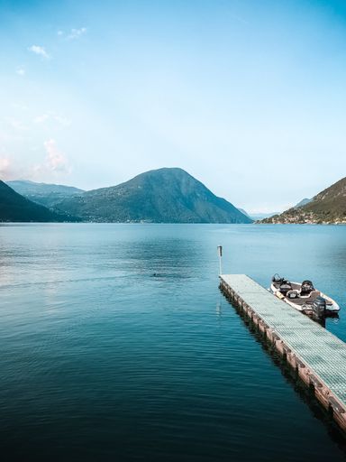A vertical shot of a boat near a wooden dock on the sea with beautiful green mountains