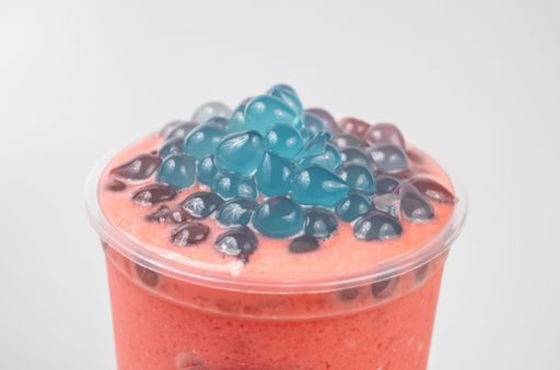 A closeup of a delicious pink bubble tea with small blue boba on top on a white background