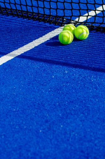 Three balls near the net of a blue padel tennis court