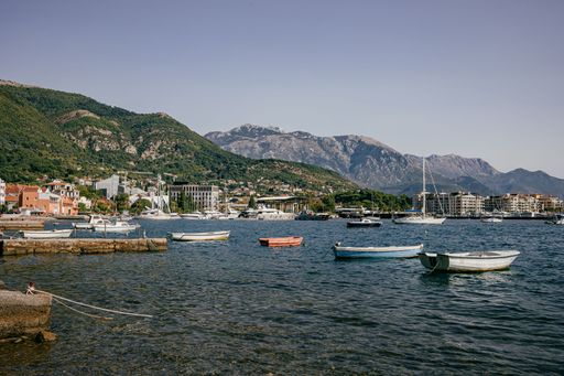 A scenic view of boats moored at the shore covered with buildings and green hills in Montenegro